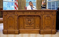 A picture of Barack Obama sitting at the Resolute Desk in the White House Oval Office.